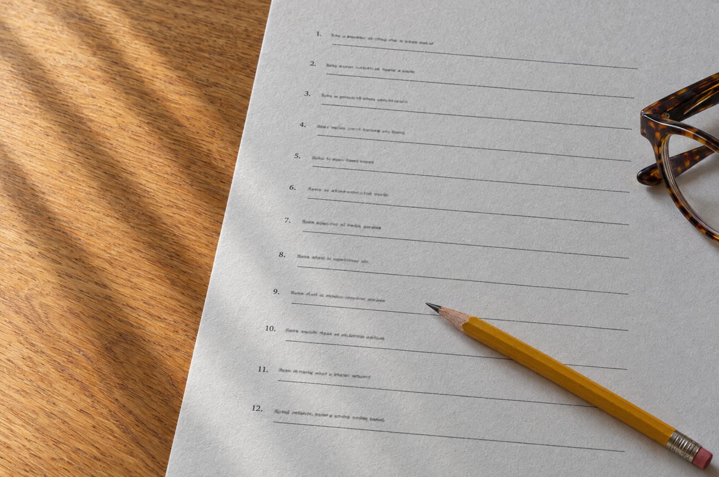 A printed worksheet with blank fill-in lines, a sharpened pencil across it, on an oak table in morning light